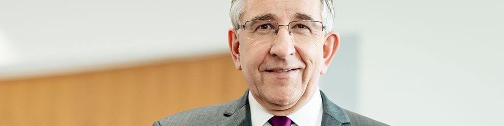 Zu sehen ist ein Mann stehend im leeren Plenarsaal.
