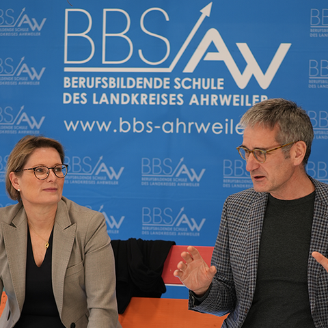 Bildungsministerin Stefanie Hubig und Landtagspräsident Hendrik Hering im Gespräch vor dem Logo der BBS Ahrweiler.