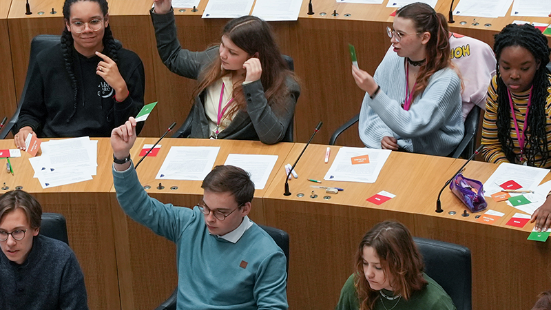 Schüler sitzen auf den Plätzen der Abgeordneten, manche von Ihnen haben ihren Arm gehoben.